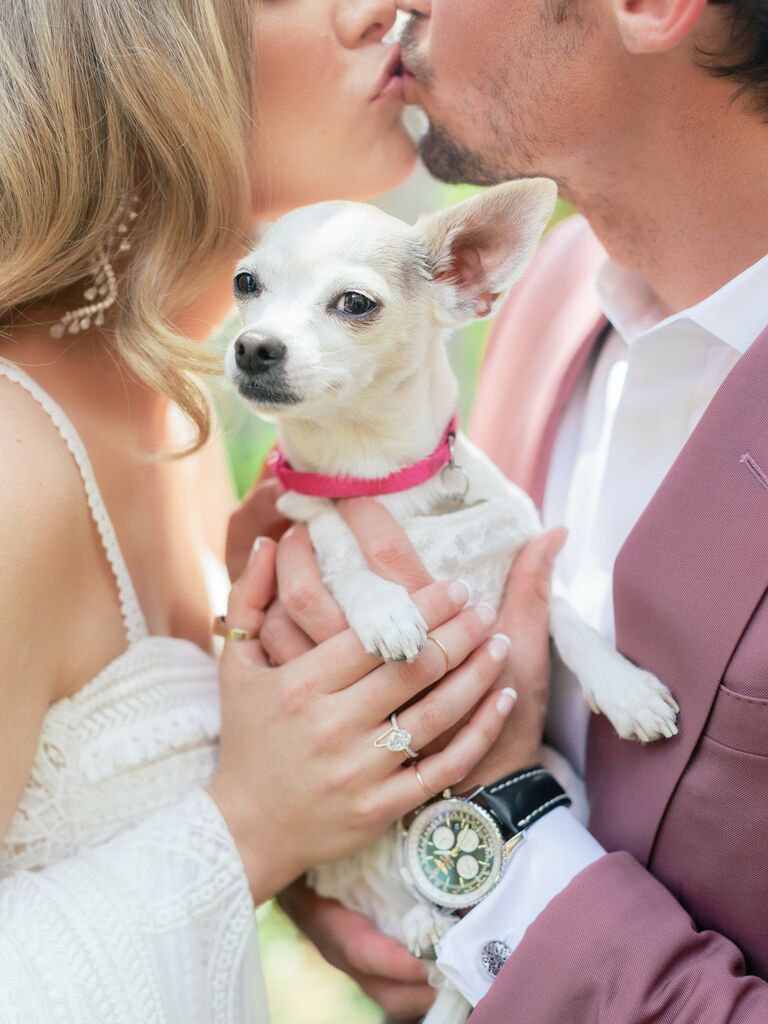 Bride and groom kissing while holding their dog. 