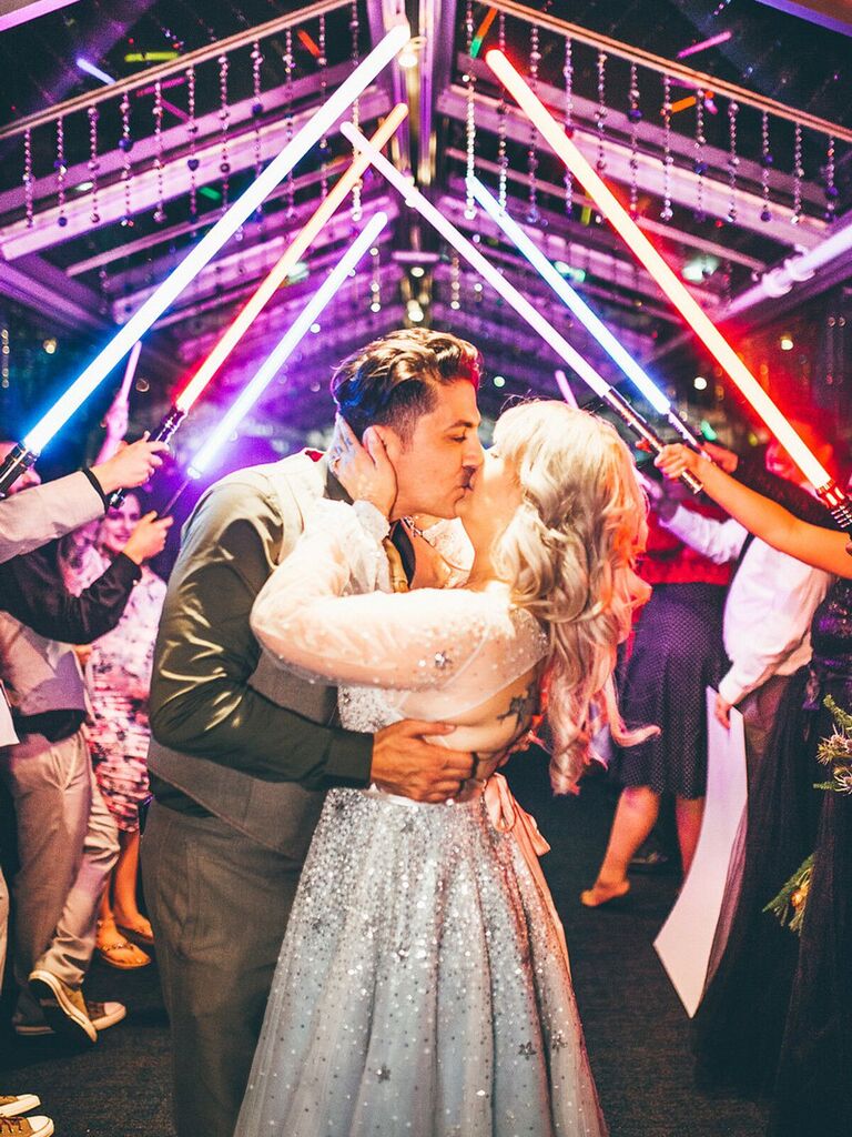 Bride and groom kissing under lightsaber arch. 