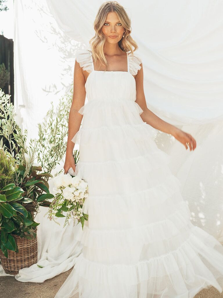 Model wears a white ruffled dress with tulle tiers. 