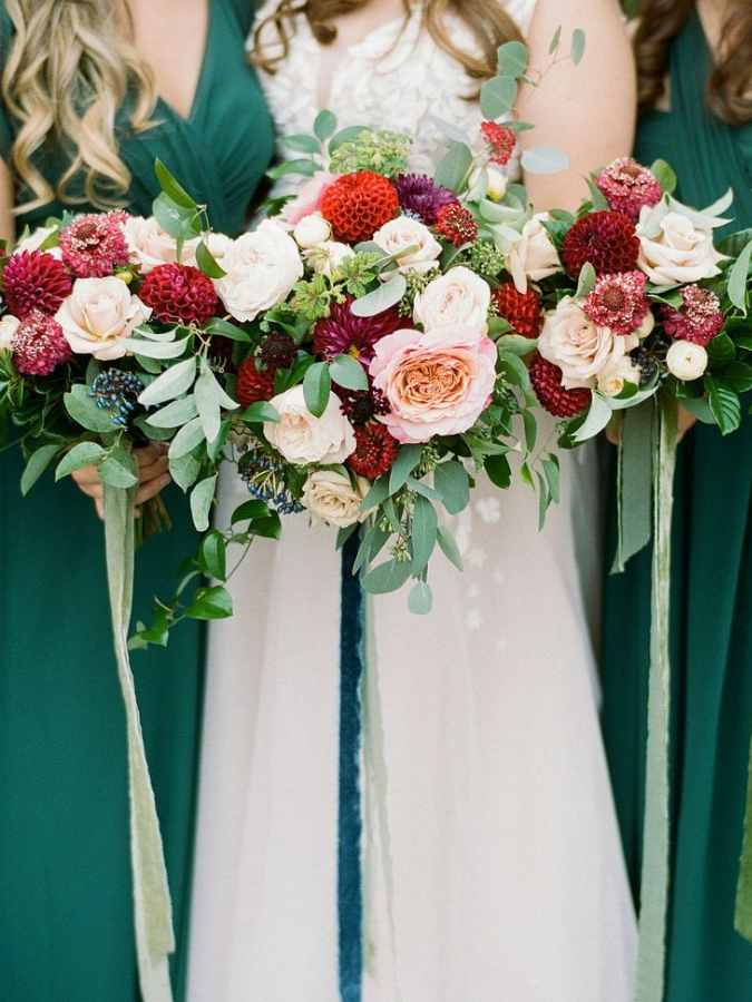 Bridesmaids in green dresses holding red dahlia bouquets