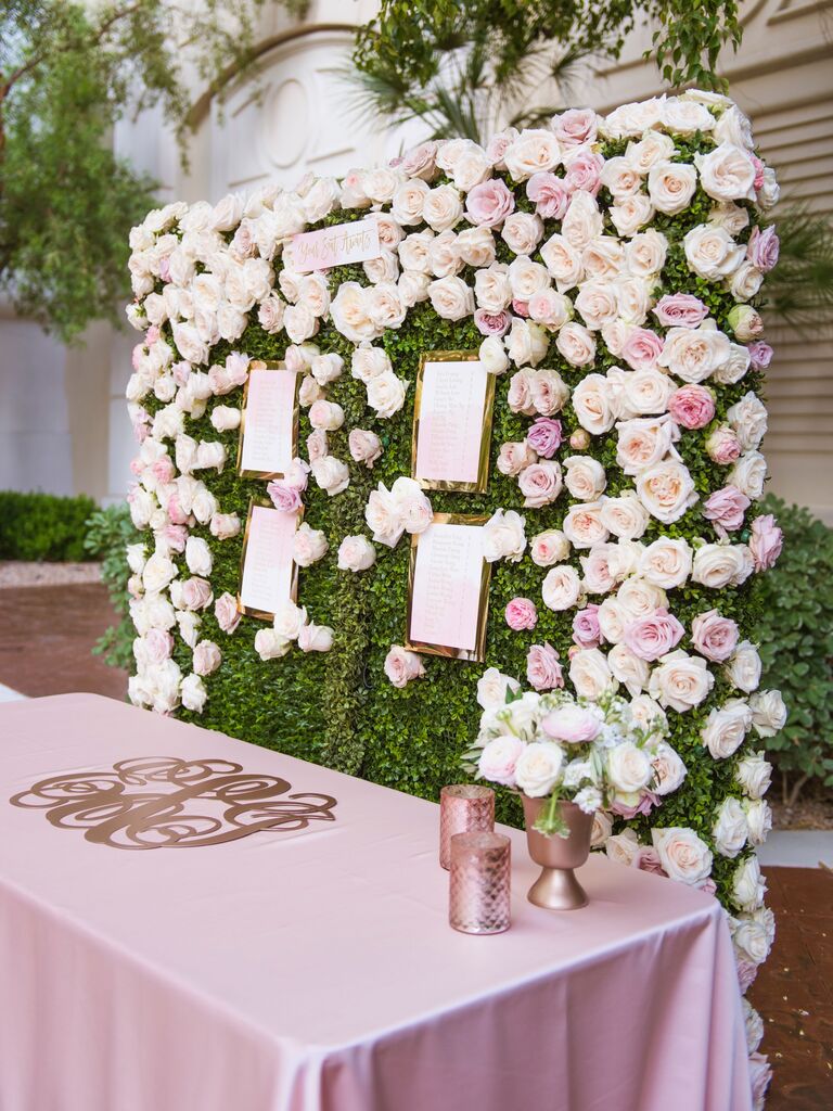 Pink and ivory rose floral wedding wall behind escort cards. 