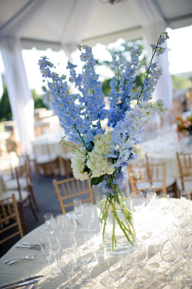 The wedding florist, Floribunda, designed three different arrangements with varying heights to decorate the reception tables. Some centerpieces incorporated coral ranunculus and lush greenery to match the bride's bouquet, while others featured white hydrangea with pops of blue delphinium in mint julep glasses.