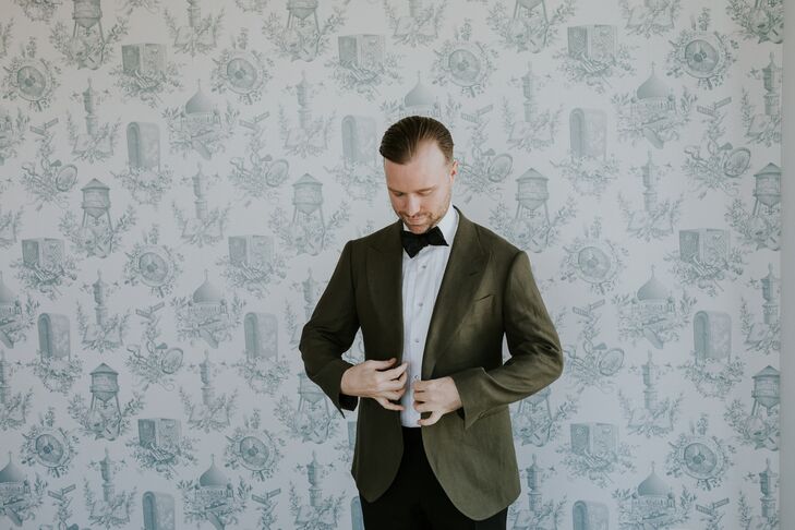 Groom Buttons Green Suit Jacket in Front of Vintage-Inspired Wallpaper