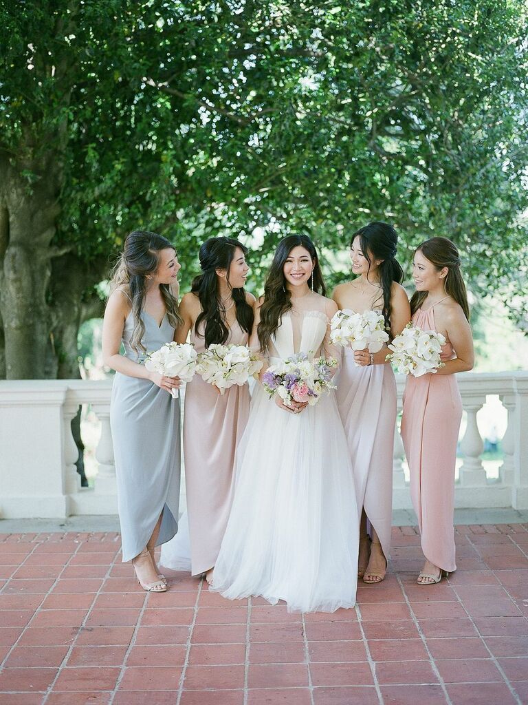 bride stands next to bridesmaids wearing mismatched pastel blue, pink and ivory floor length dresses