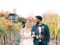 Black bride wearing mermaid wedding dress walks with groom through vineyard