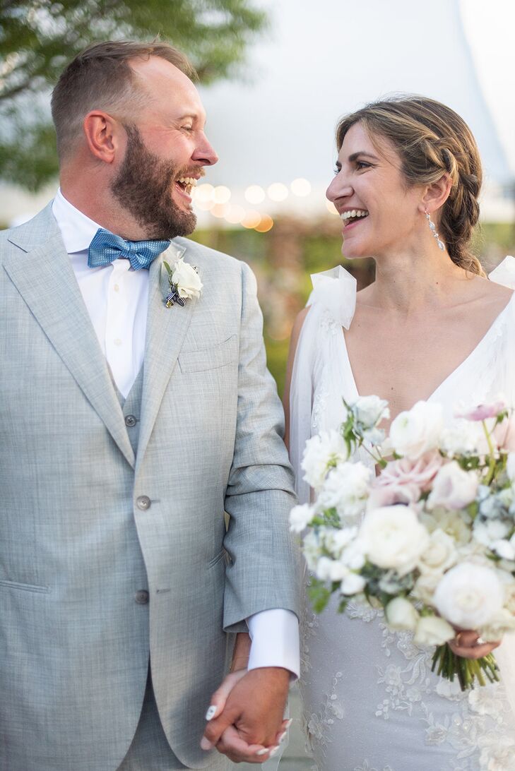 Groom in Light Gray Suit and Blue Bow Tie Smiling at Bride With Braided Hair, Light Bouquet