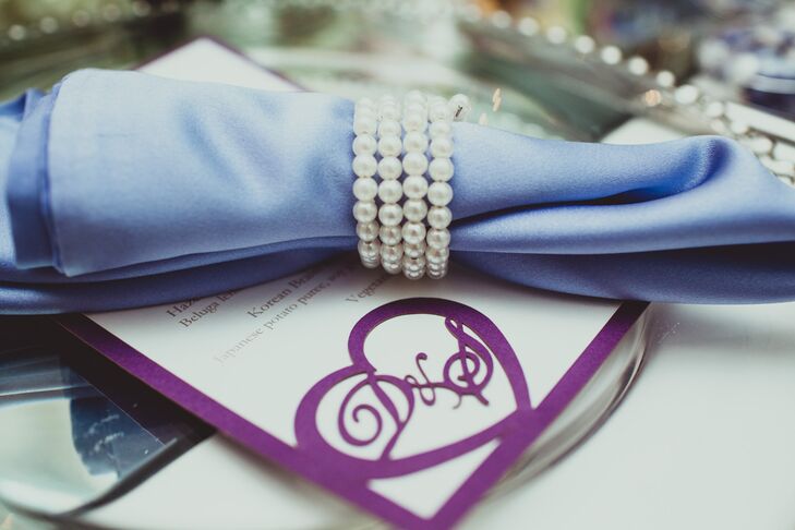 The white menu card was accented with a purple heart design that displayed the couple's initials, which matched the border of the stationery. A napkin in a different shade of purple was held together by a pearl ring and placed on top of the menu.