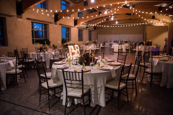 At the indoor, on-site reception at Springs Preserve in Las Vegas, Nevada, candelabras were placed around the floral centerpieces to add ambience. Wooden, free-standing numbers were placed on each table for guests to find their seats.