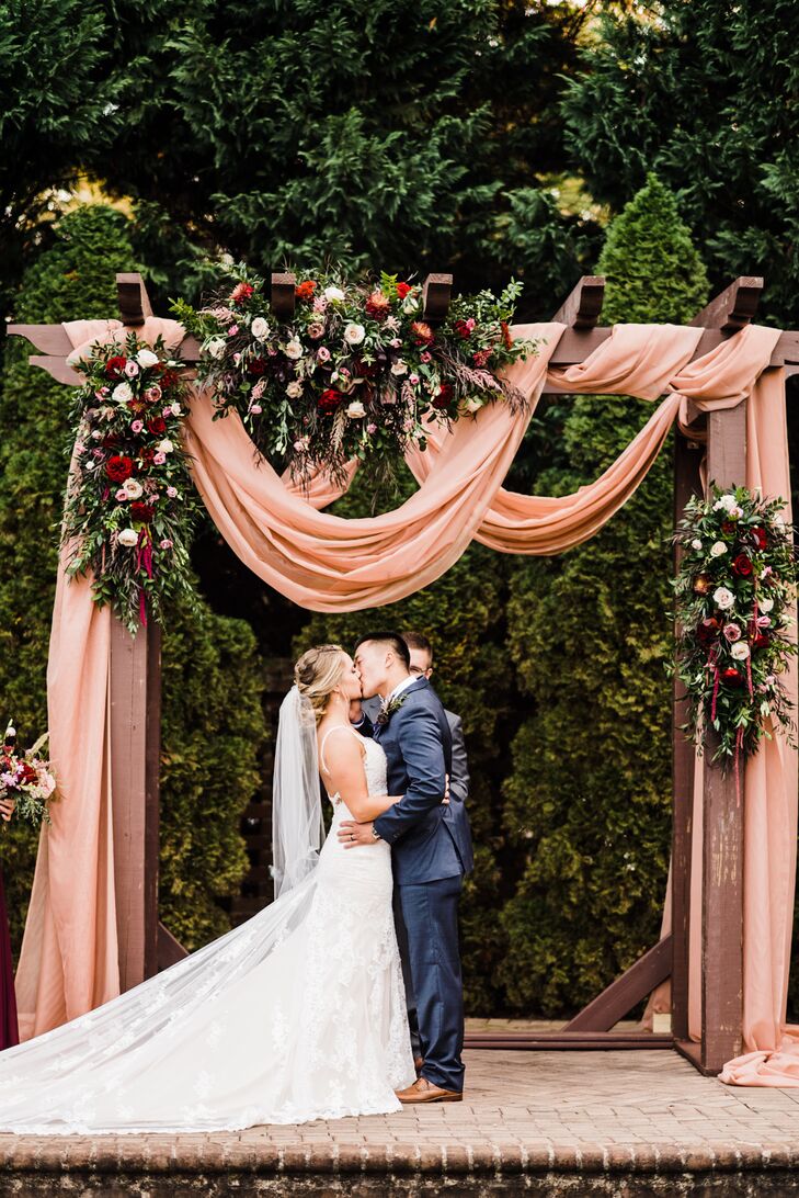 Couple Under Wedding Arch with Pink Draping, Roses and Greenery