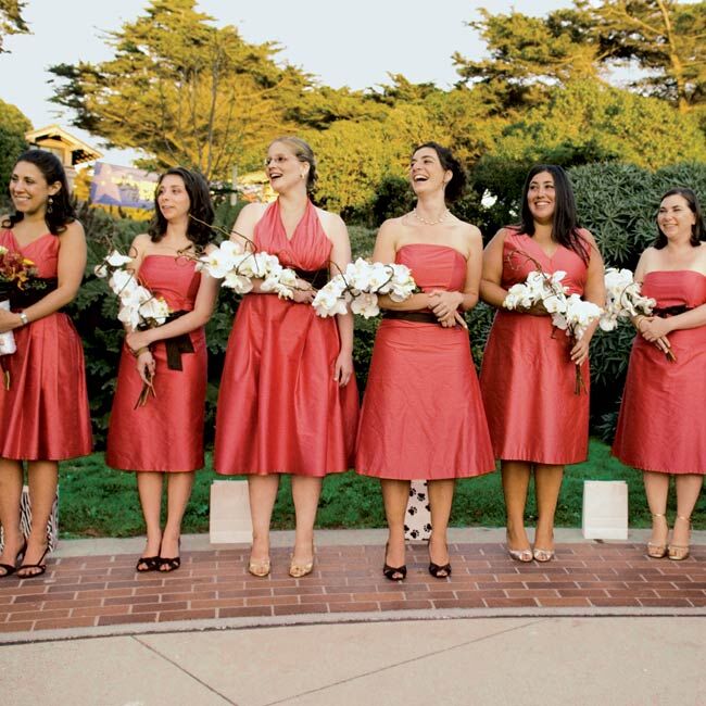 Emily's eight bridesmaids chose guava-colored tea-length dresses with brown sashes in various styles. Each carried large bouquets of branches wrapped with oversized white orchids.