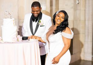 Bride in Off-the-Shoulder Gown and Groom in White-and-Black Tuxedo Jacket Cut Two-Tier Cake