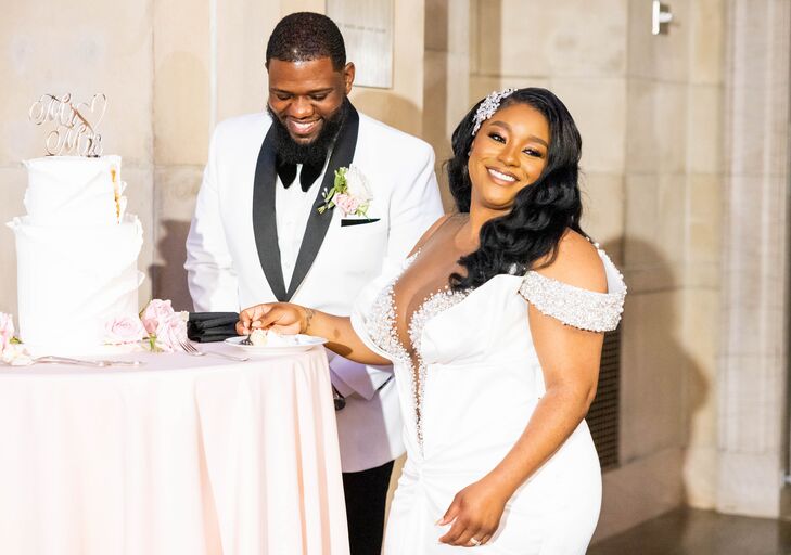Bride in Off-the-Shoulder Gown and Groom in White-and-Black Tuxedo Jacket Cut Two-Tier Cake