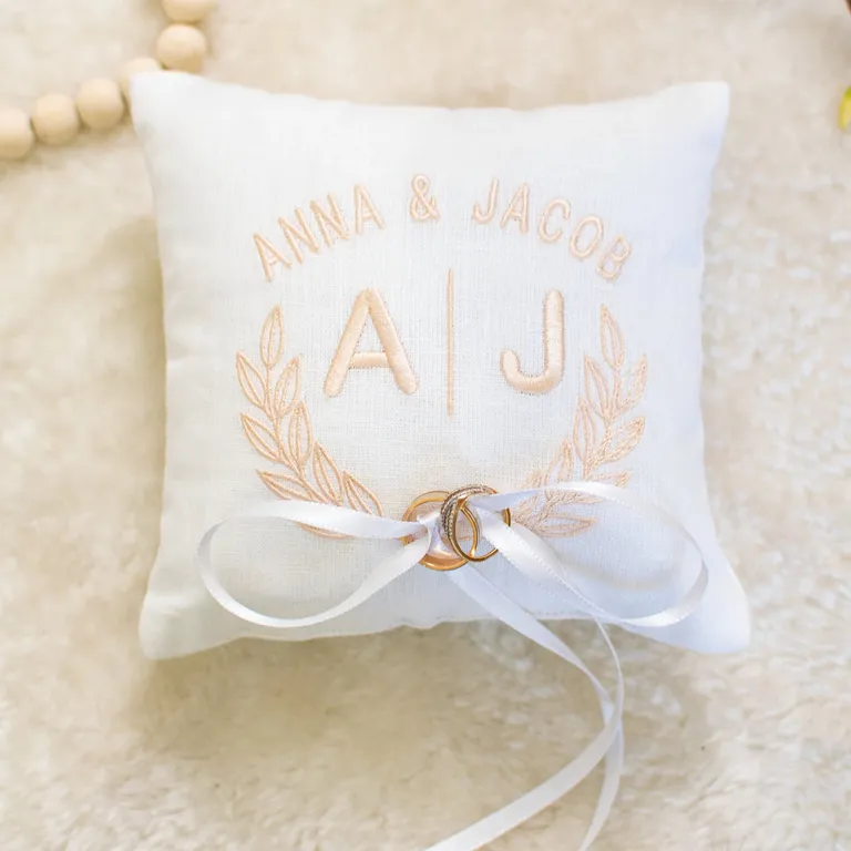 White linen ring bearer pillow with light pink monogram and laurel wreath