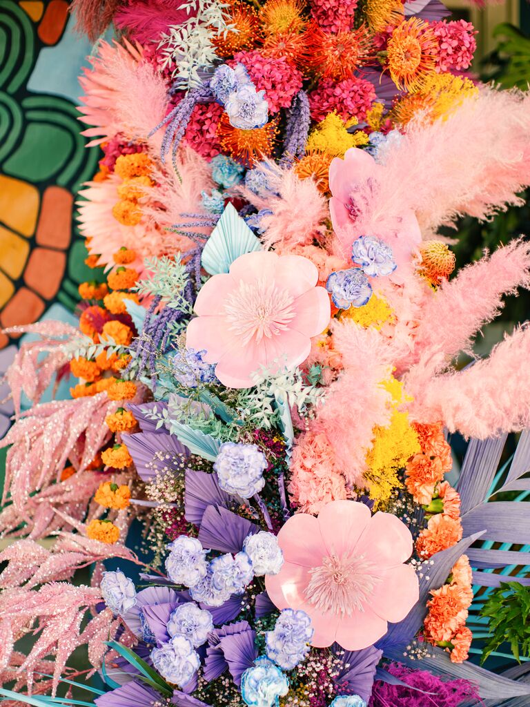 closeup of wedding flower installation with oversized paper flowers, glittery branches, dried greenery and pampas grass in rainbow color palette