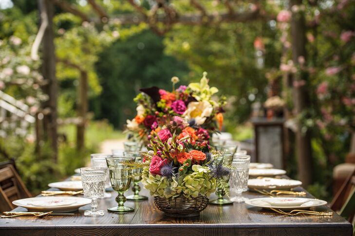 The long wooden reception table was style by Simply Styled with vintage place settings, elegant colored glasses and vibrant floral arrangements by Chelish Moore Flowers that added a pop of color to the rustic setting.