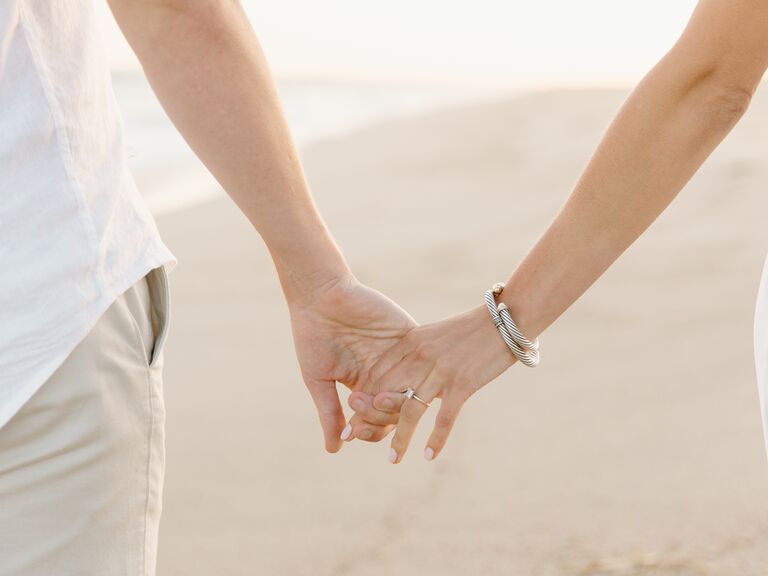 Couple holds hands on a beach. 