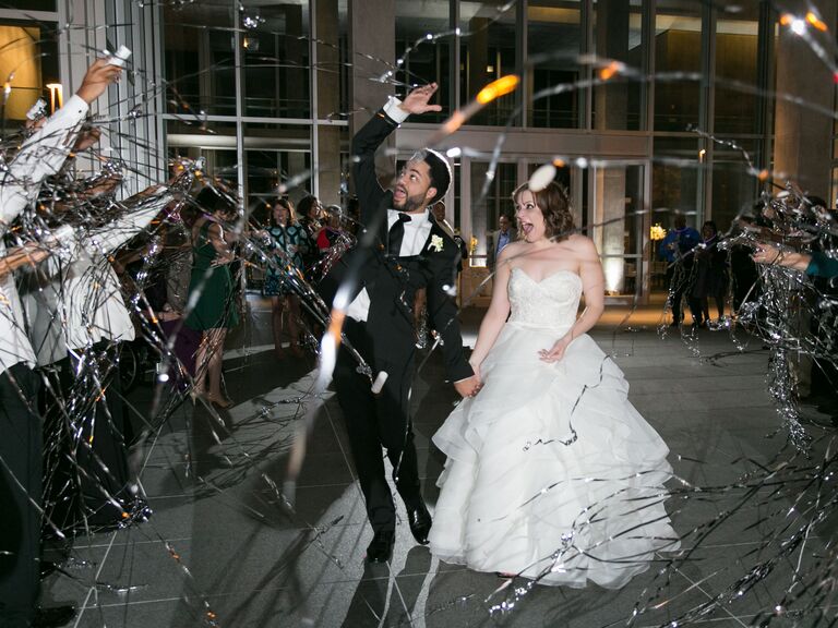 Bride and grooms stroll through streamers for wedding send-off. 