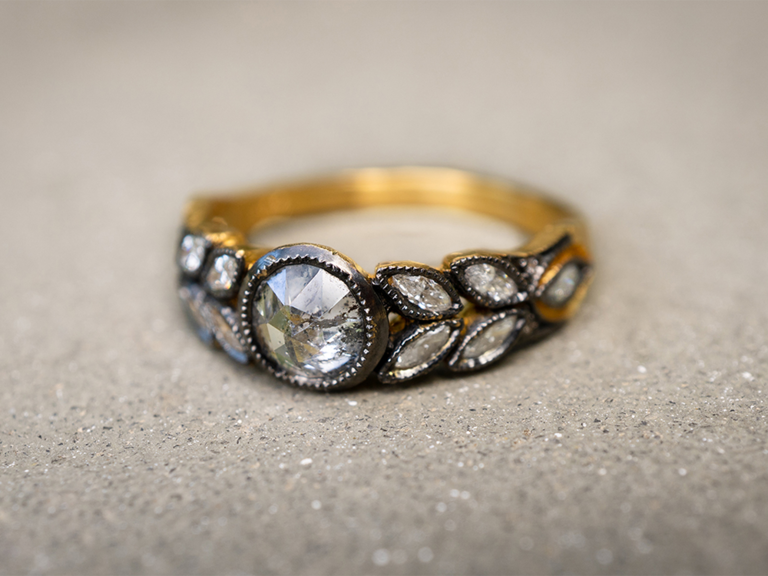 Round cut center diamond with black border and marquise cut diamonds on sides of gold band