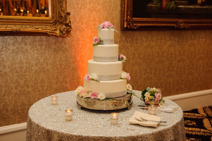 The four-tier white wedding cake was wrapped with silver at the bottom of each tier. The cake was accented with fresh flowers on top and on the sides, and was positioned on a silver cake stand.