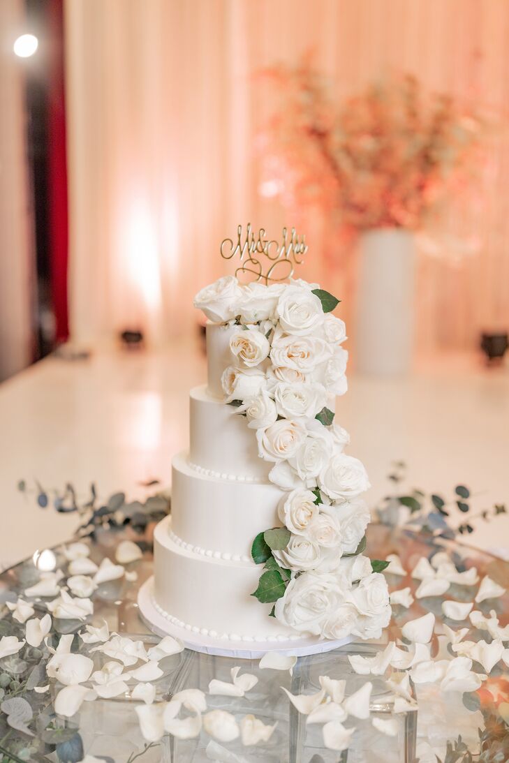 Four-Tier White Wedding Cake With Cascading White Flowers, Gold Toppers