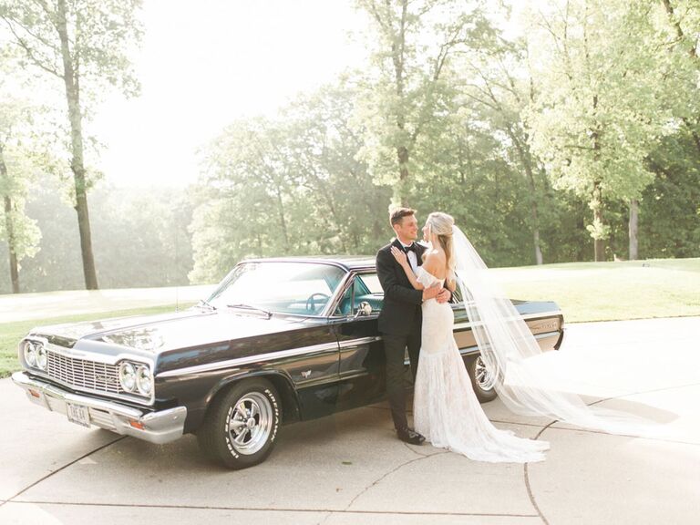 Bride and groom in front of black vintage getaway car