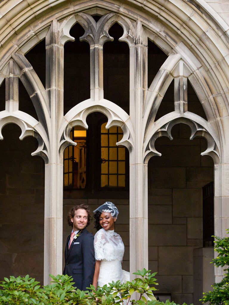 Groom posing with bride wearing vintage lace capelet and blusher veil