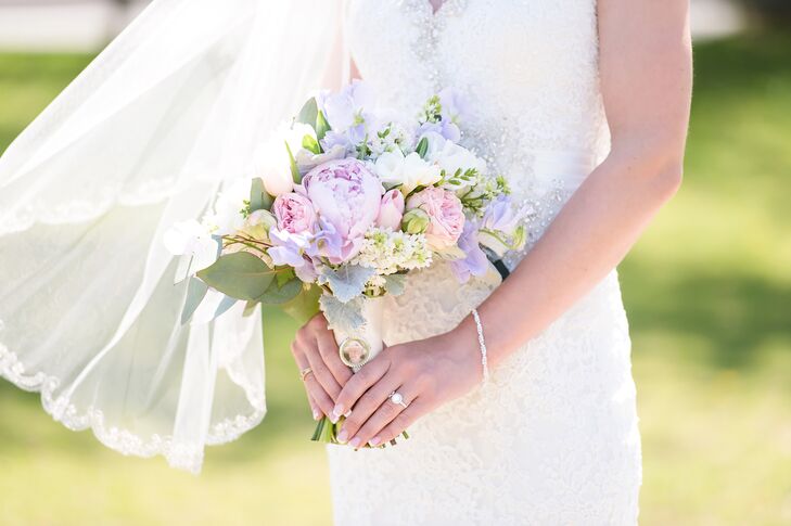 Her bouquet was the picture of spring. She carried a lush arrangement of purple peonies, purple delphiniums, pink garden roses, pink tulips, white peonies, greenery, dusty miller and eucalyptus. The ivory ribbon wrap added a sentimental touch with a personal photo charm on the front.