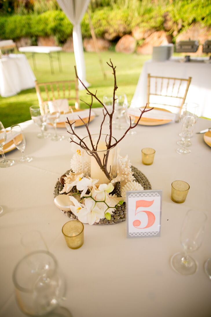 Centerpieces of white candles surrounded by seashells and branches decorated the dining tables at the reception. White and silver paper displayed table numbers printed in a coral color.