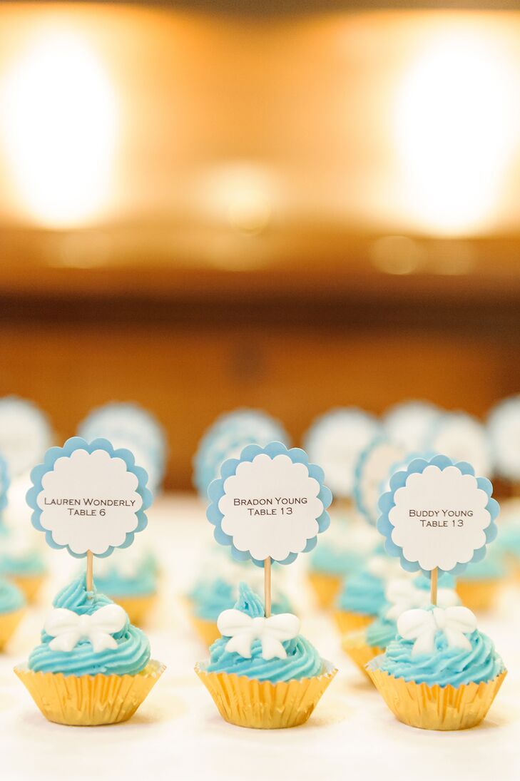 The scalloped escort cards with light blue trim were displayed on min cupcakes baked by Erin. The cupcakes were decorated with light blue frosting and white fondant bows.