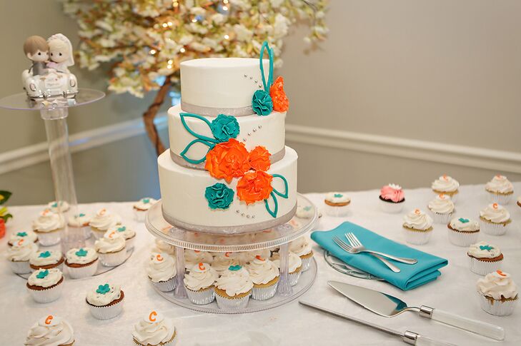 The three tier ivory wedding cake was decorated with orange and turquoise fondant flowers and surrounded by cupcakes. The flavor was almond vanilla cake with raspberry preserve filling. The Precious Moments cake topper featured a loving couple in their getaway car.
