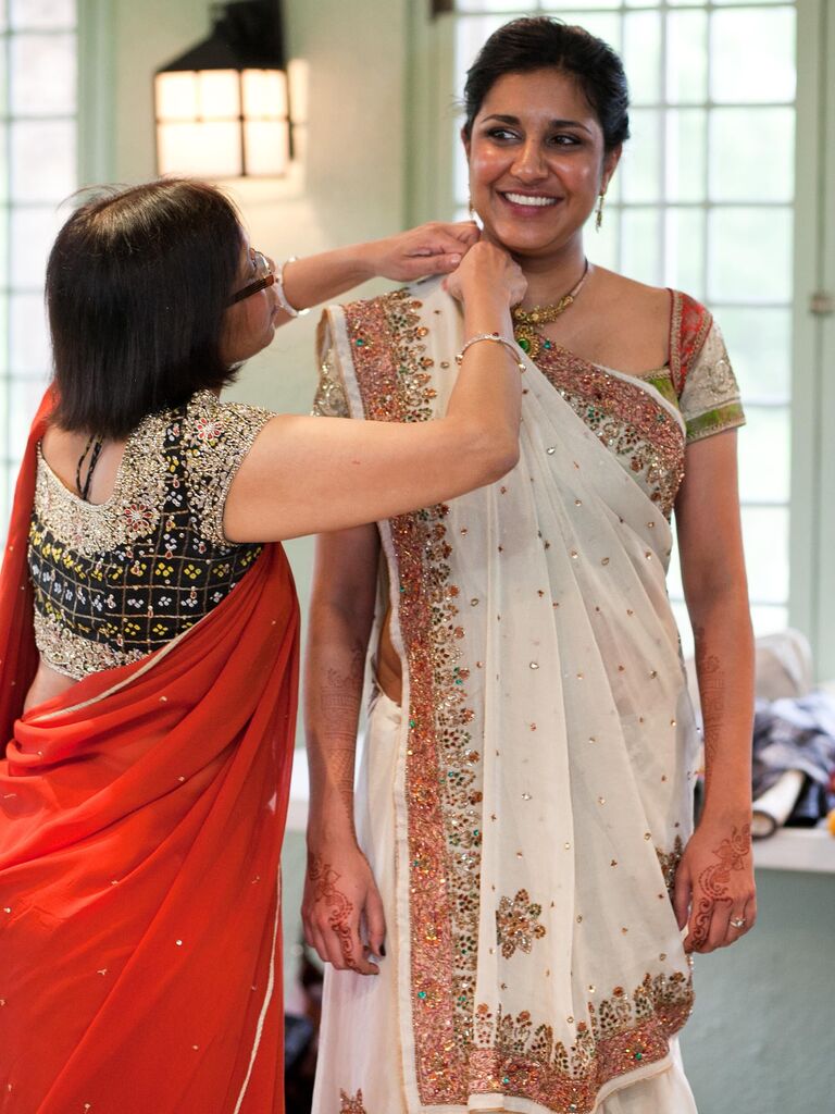 Bride gets help draping white wedding saree before ceremony.