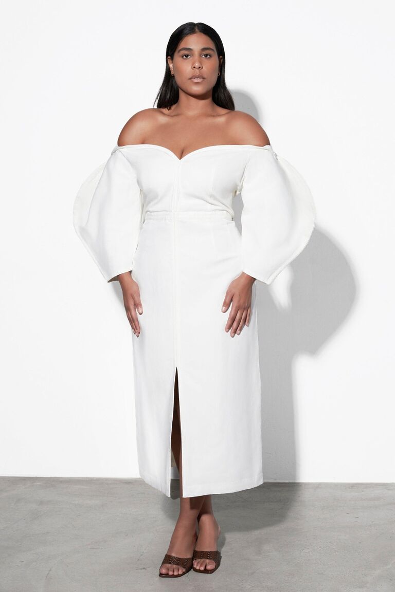 Model wears an off the shoulder white dress with puffed sleeves. 
