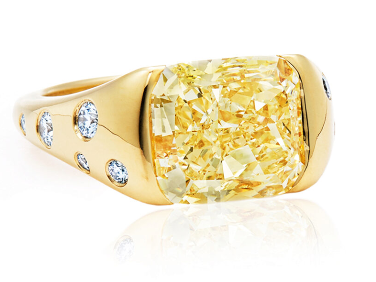 Yellow cushion cut diamond center on thick gold tapered band with diamonds on side