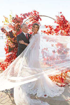 Bride With Windswept Tulle Cape With Groom in Classic Suit an Red Leaf Arch