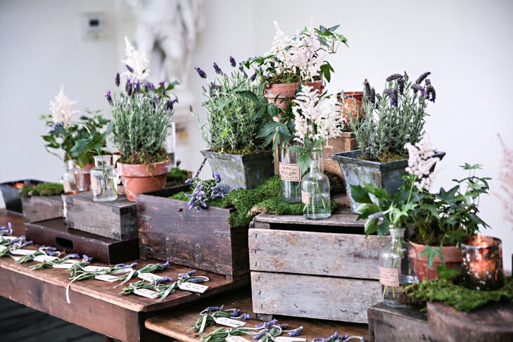 Escort cards made by The Papery were assembled on a wooden farmhouse table, surrounded by wood boxes with astilbe and lavender in pots and glass vases, created by TableArt.