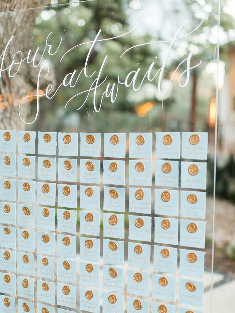 wedding escort card display with pastel blue cards and gold wax seals on clear acrylic board 