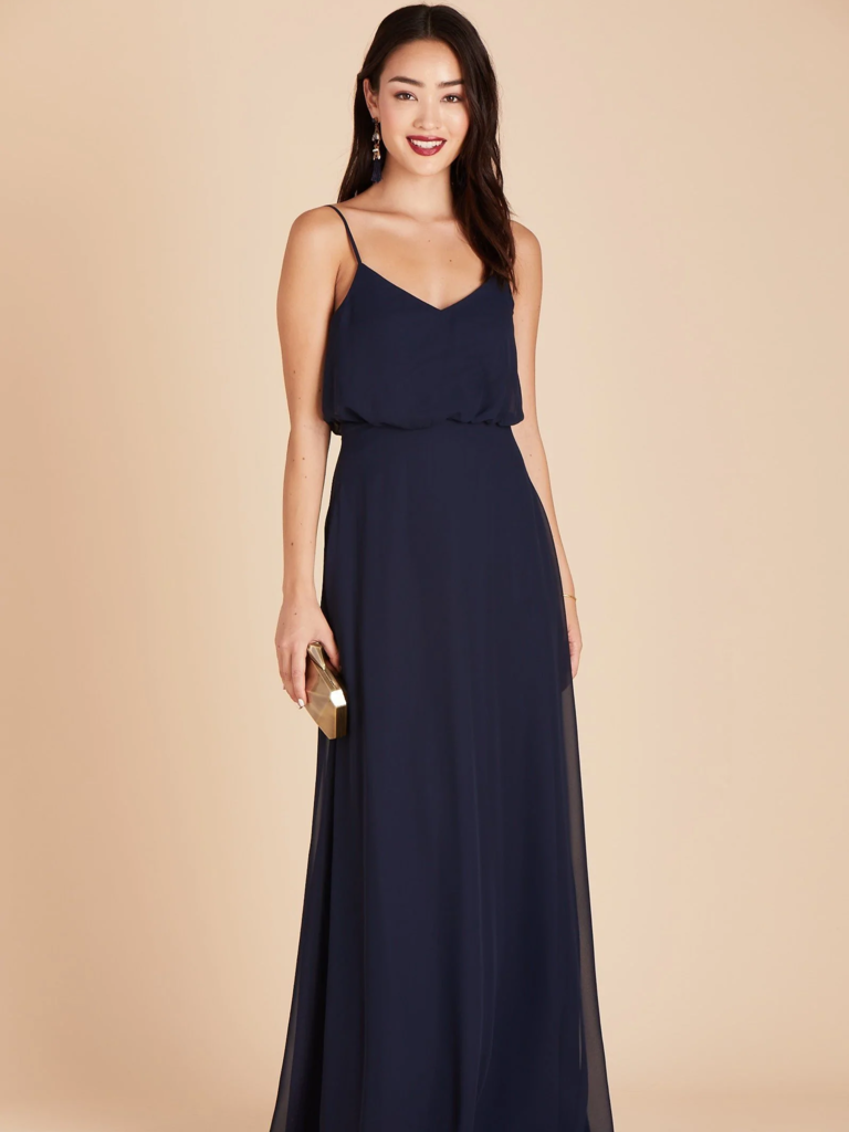 A model wears a spaghetti strap bridesmaid gown, carrying a clutch.
