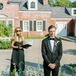 Officiant in Black Gown and Groom in Black Tux Waiting for Bride at Outdoor Altar, Gravel, Pastel Flowers