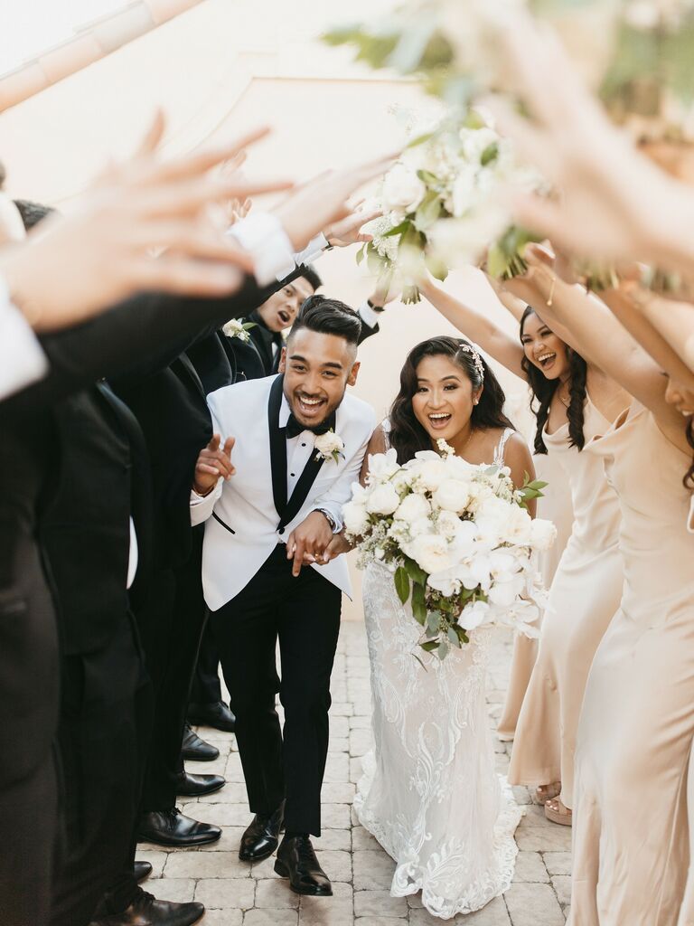Bride and groom walking under tunnel of guests' arms.