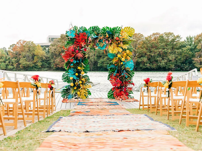 This modern tropical wedding arch is complemented by shabby-chic rugs along the aisle.