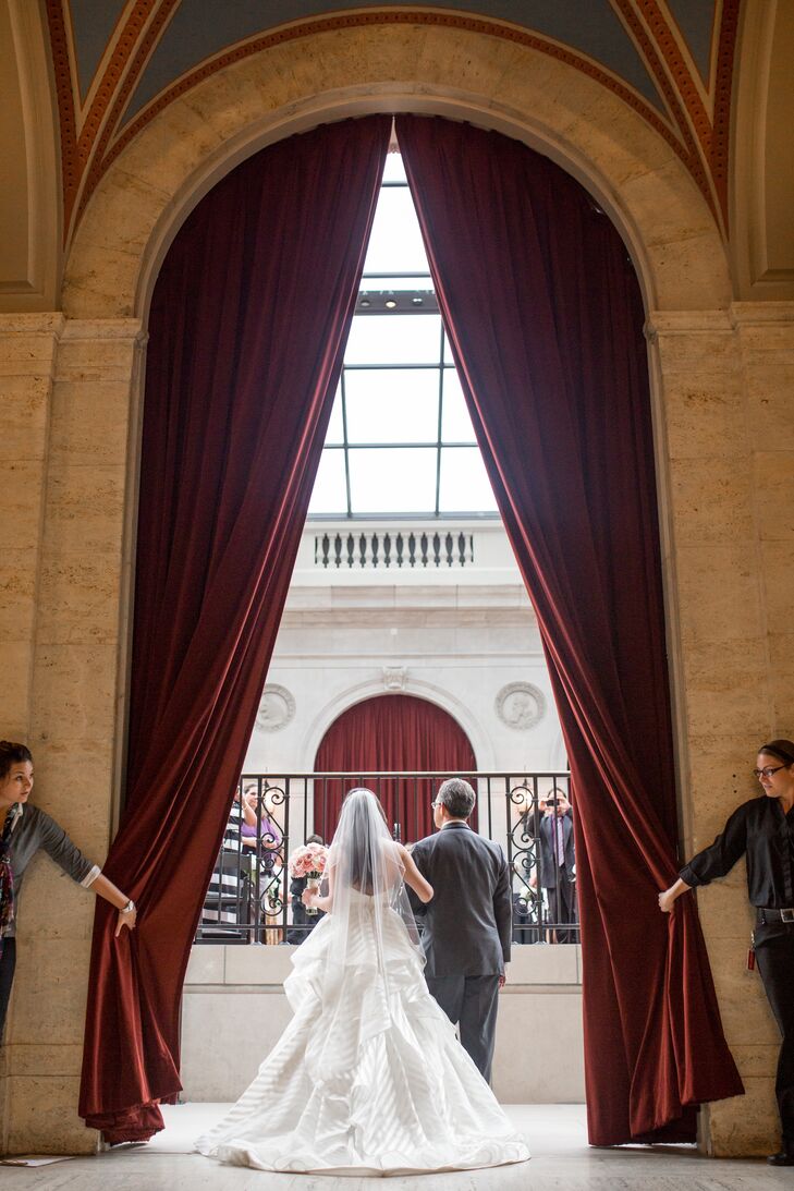 Elon entered the ceremony through deep red draped curtains on her father's arm, which took place inside the Columbus Museum of Art in Columbus, Ohio. Elon was walked down the aisle in her ivory strapless wedding dress designed by Hayley Paige, complemented by her traditional ivory tulle veil in her long hairstyle.