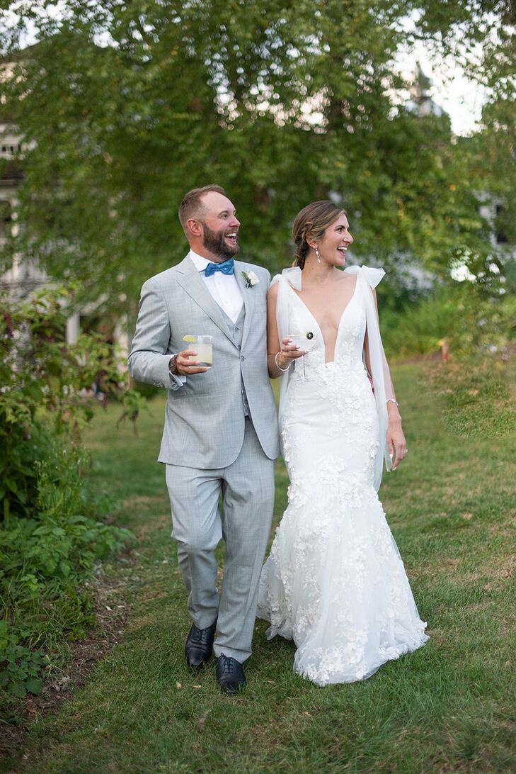 Groom in Light Gray Suit and Blue Bow Tie With Bride in Fitted Gown Carrying Cocktails