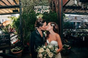 Bride in White Gown and Bride in Black Blazer, Simple Bouquet, Kiss in Front of Custom Sign, Greenery on Rooftop