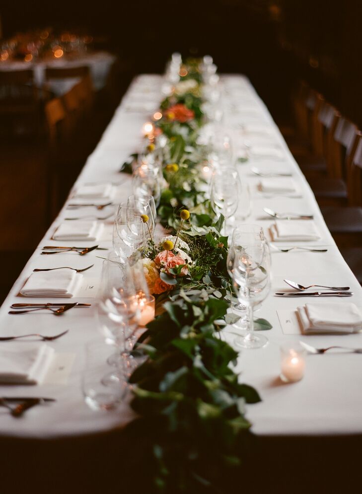 Each reception table boasted a centerpiece, with the head table displaying a long lush garland of textured greenery, cheerful craspedia and roses in shades of ivory and coral. Offset by flickering votive candles, the chic centerpiece helped establish an intimate ambiance during the meal.