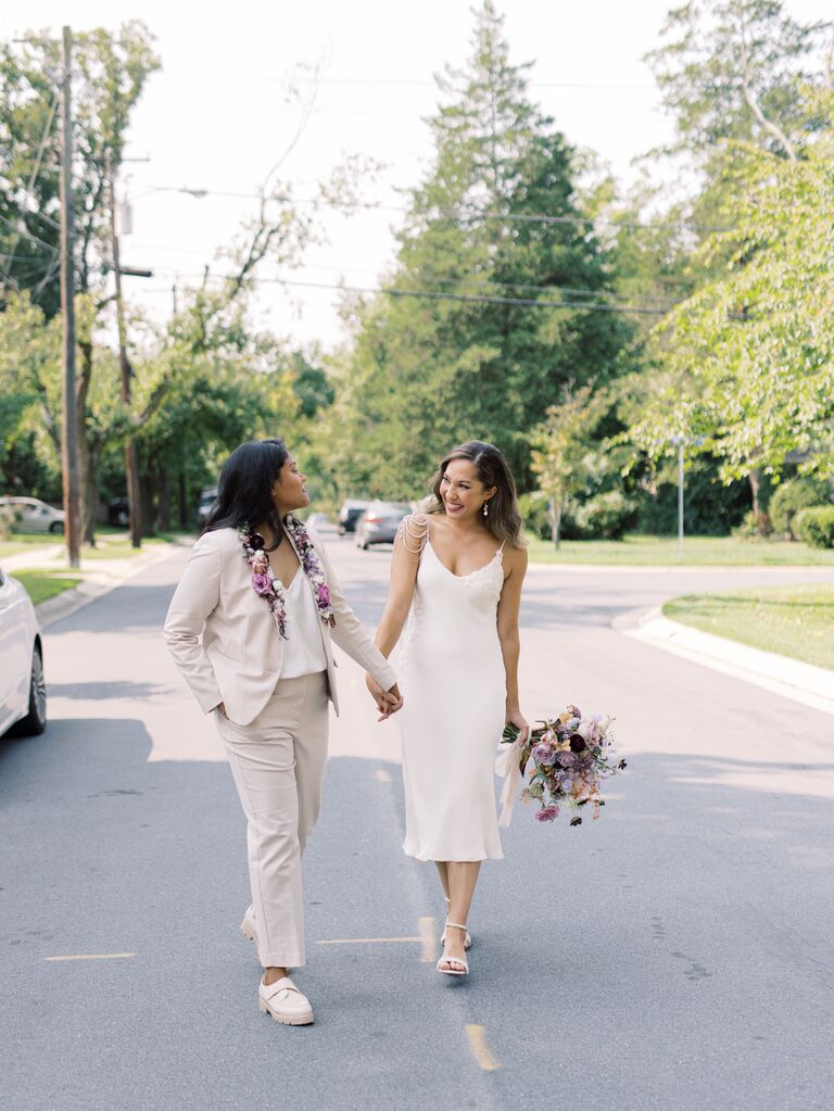 A wedding couple hold hands while they walk down the road together