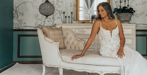 Bride in spaghetti strap lace wedding gown sitting on a chaise lounge