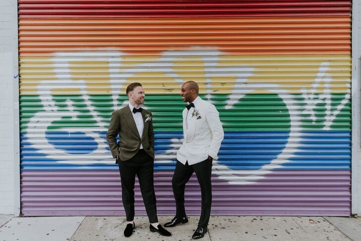 Two Grooms in Different Suits Pose in Front of Rainbow Wall