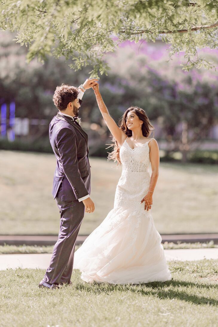 Groom in Navy Tuxedo Twirls Bride in Lace Trumpet Wedding Dress on a Lawn