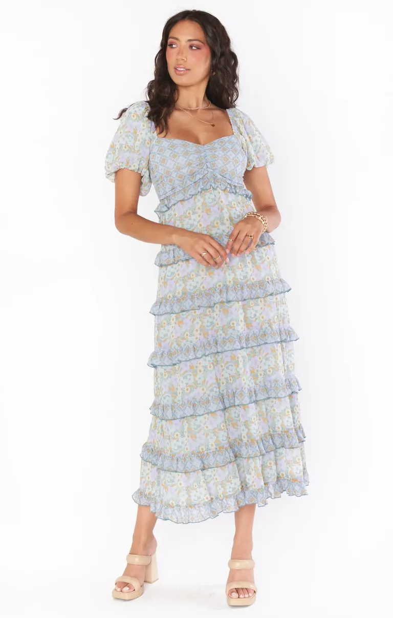 Model wears a pastel blue gown with a ruffled hem and floral pattern. 