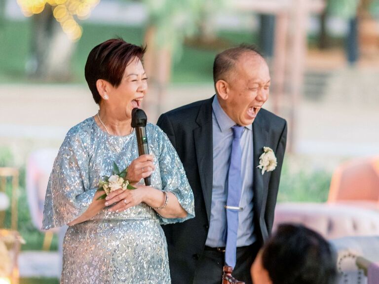 Parents of the bride laugh while giving a heartfelt wedding speech. 